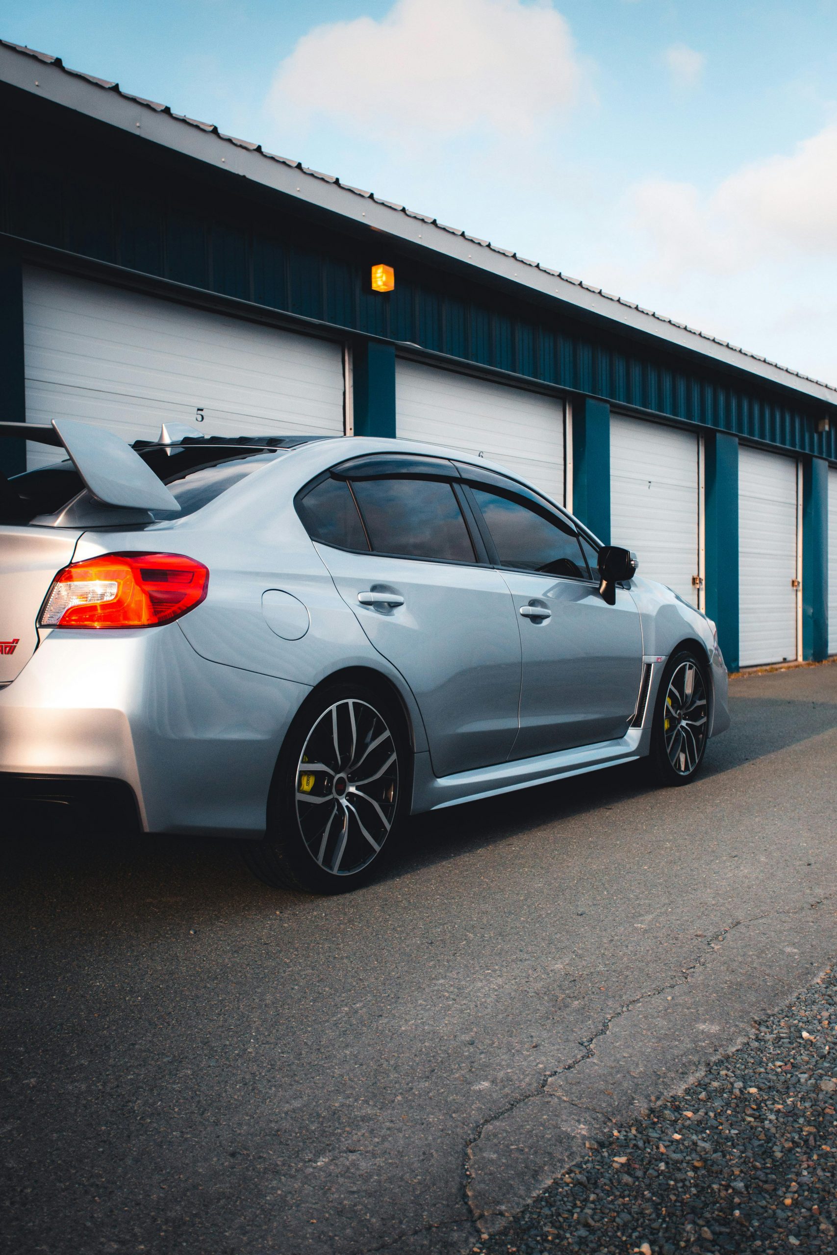 Silver sports car parked outside blue and white garage during daytime.