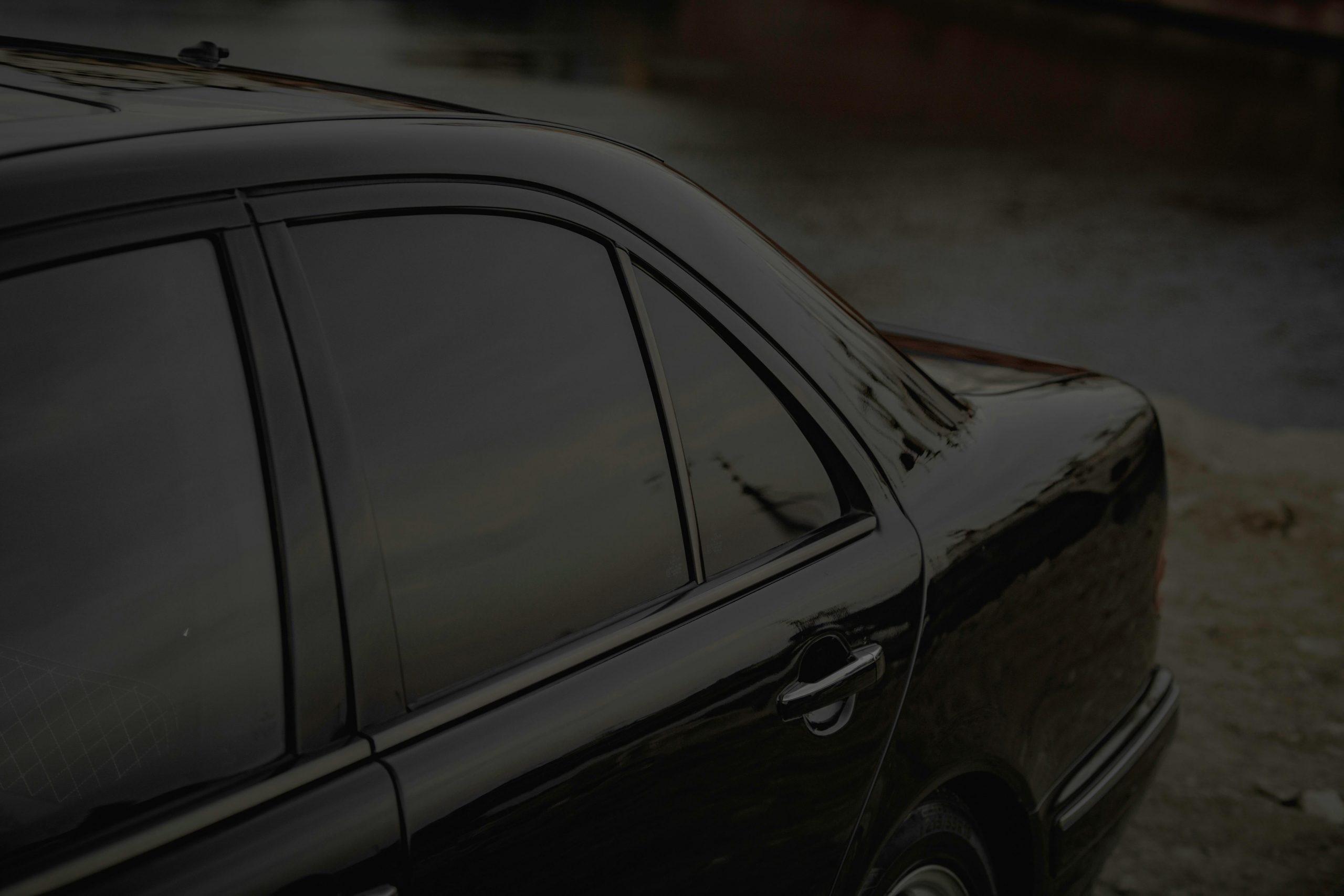 Close-up of a black car's side view with tinted windows by a calm riverbank.